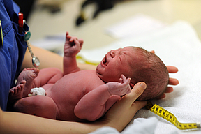 Neugeborenes liegt auf den Armen einer Person, die es vermisst, mit Maßband neben dem Baby
