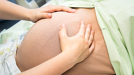 Hände legen sich auf einen schwangeren Bauch-Dummy unter einem grünen Tuch