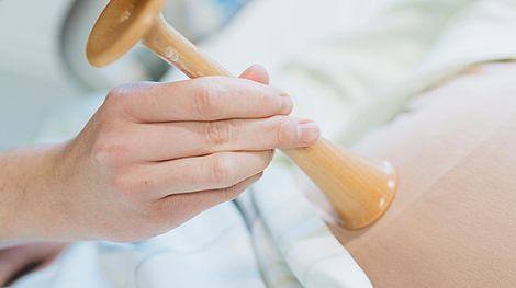 Hand hält ein hölzernes Stethoskop auf einem Bauch