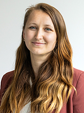 Frau mit langen gewellten Haaren und rotem Blazer vor weißem Hintergrund